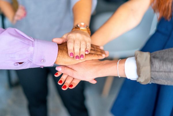 Imagem que representa o que é filantropia cinco pessoas de diferentes origens unem as mãos, simbolizando solidariedade, diversidade e colaboração em ações coletivas voltadas ao bem comum e apoio comunitário.